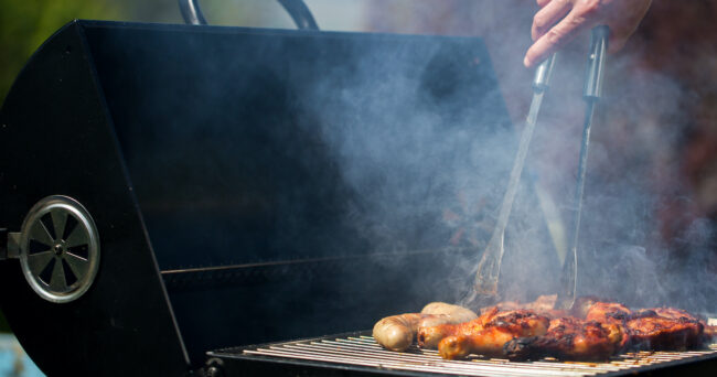 Young man grills some kind of marinated meat and vegetable on gas grill during summer time gas grilling food